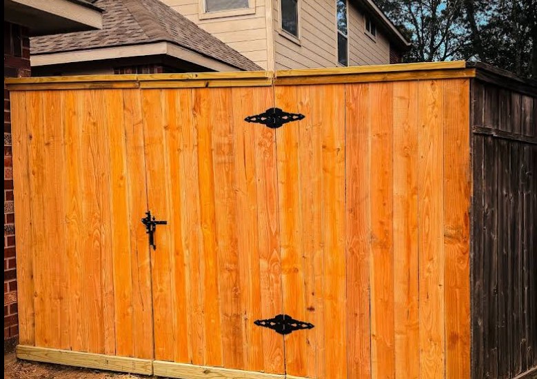 Freshly stained cedar privacy fence with double gate and decorative hinges — Gomez Fencing